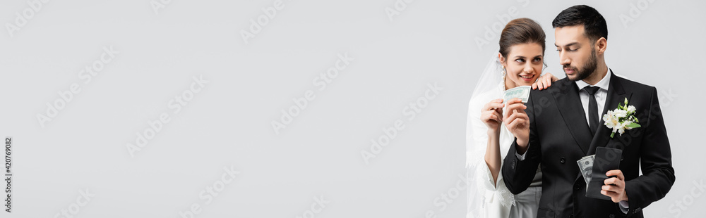 Arabian groom in suit giving cash to smiling bride isolated on grey, banner Arabian groom in suit giving cash to smiling bride isolated on grey, banner