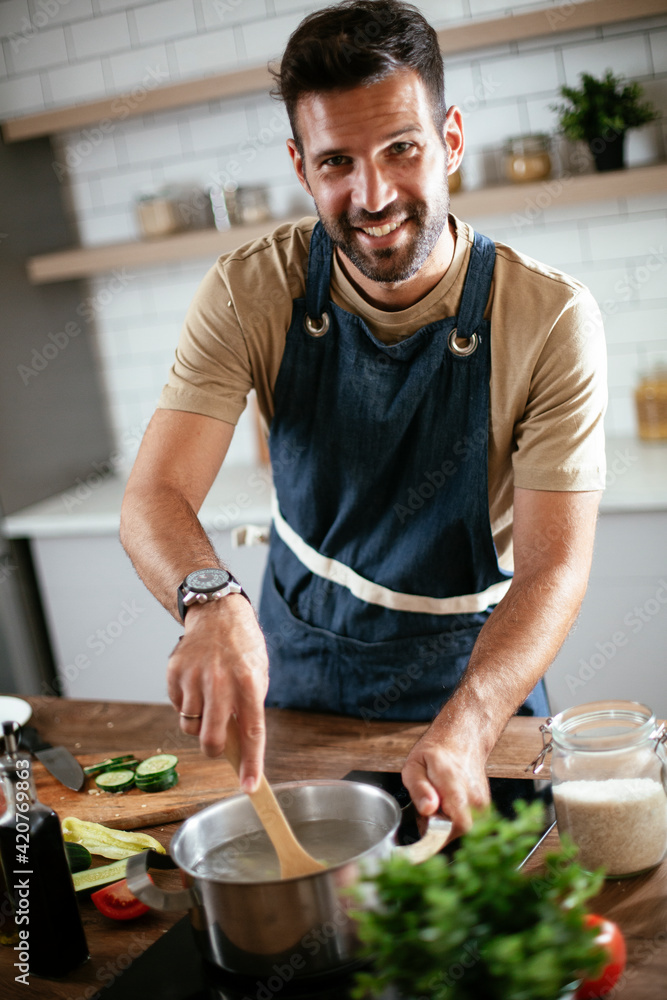 Happy smiling man preparing tasty meal. Young man cooking in the kitchen.. Happy smiling man preparing tasty meal. Young man cooking in the kitchen..