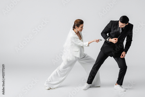 Young bride pulling handcuffs on hand of muslim boyfriend on white background