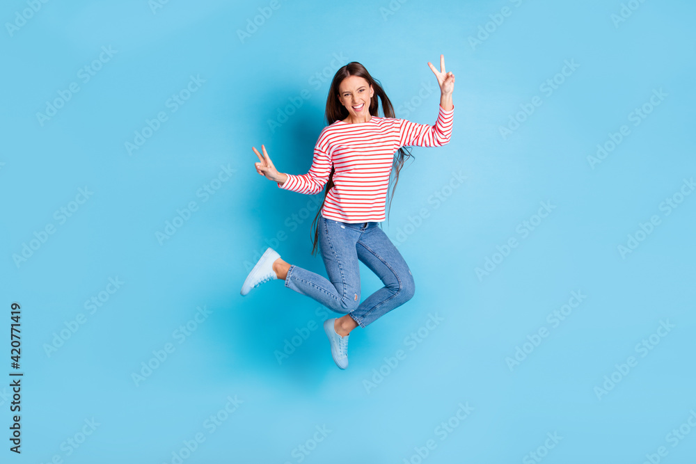 Full length body size photo jumping girl showing v-sign gesture with both hands smiling isolated vivid blue color background