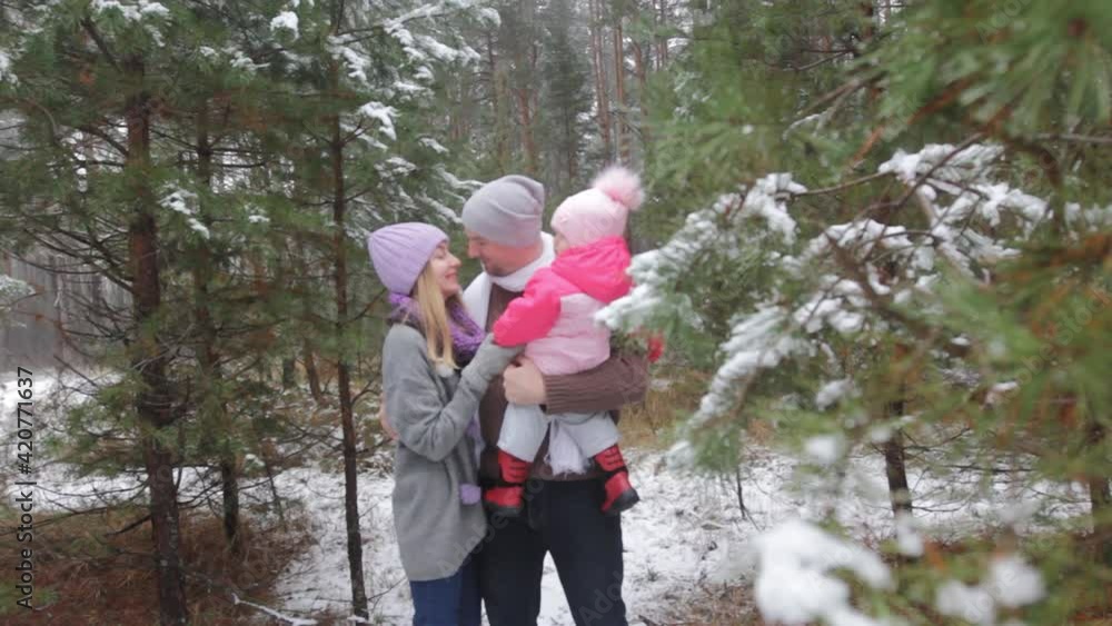 a happy married couple embrace each other and a child while among the snow-covered fir trees in the winter forest a happy married couple embrace each other and a child while among the snow-covered fir trees in the winter forest