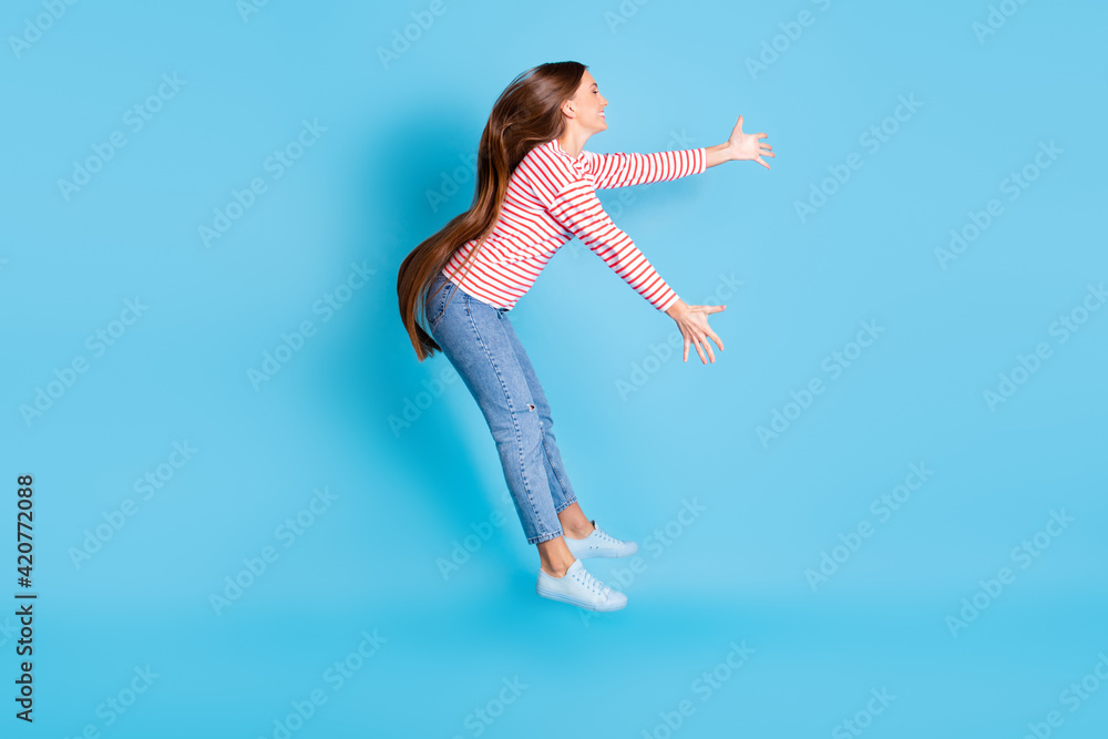 Full length body size side profile photo girl jumping flying cyclone strong wind isolated vibrant blue color background Full length body size side profile photo girl jumping flying cyclone strong wind isolated vibrant blue color background