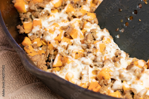 Ground turkey meat, cubed sweet potatoes, melted mozzarella cheese, and diced onions served for dinner in a cheesy, nutritious cast iron skillet meal in a home kitchen.