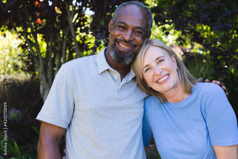 Portrait of diverse senior couple in garden looking at camera and smiling Portrait of diverse senior couple in garden looking at camera and smiling