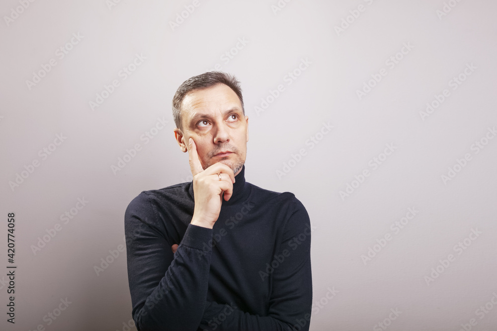A white middle aged man of European appearance with gray in his hair and a slightly unshaven face in a black turtleneck looks up thoughtfully resting his chin on his hand A white middle aged man of European appearance with gray in his hair and a slightly unshaven face in a black turtleneck looks up thoughtfully resting his chin on his hand