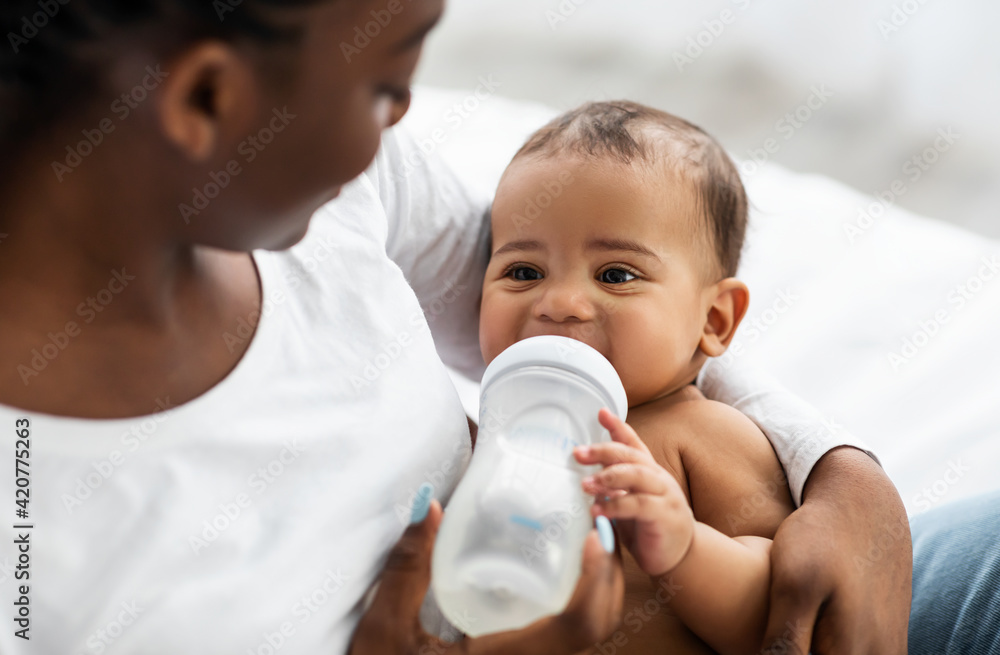 African American woman feeding her child from baby bottle African American woman feeding her child from baby bottle