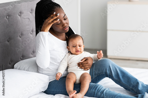 Tired African American mom sitting with kid on bed photo