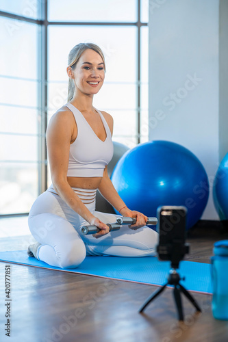 Cheerful female fitness blogger records exercises with dumbbells on smartphone camera