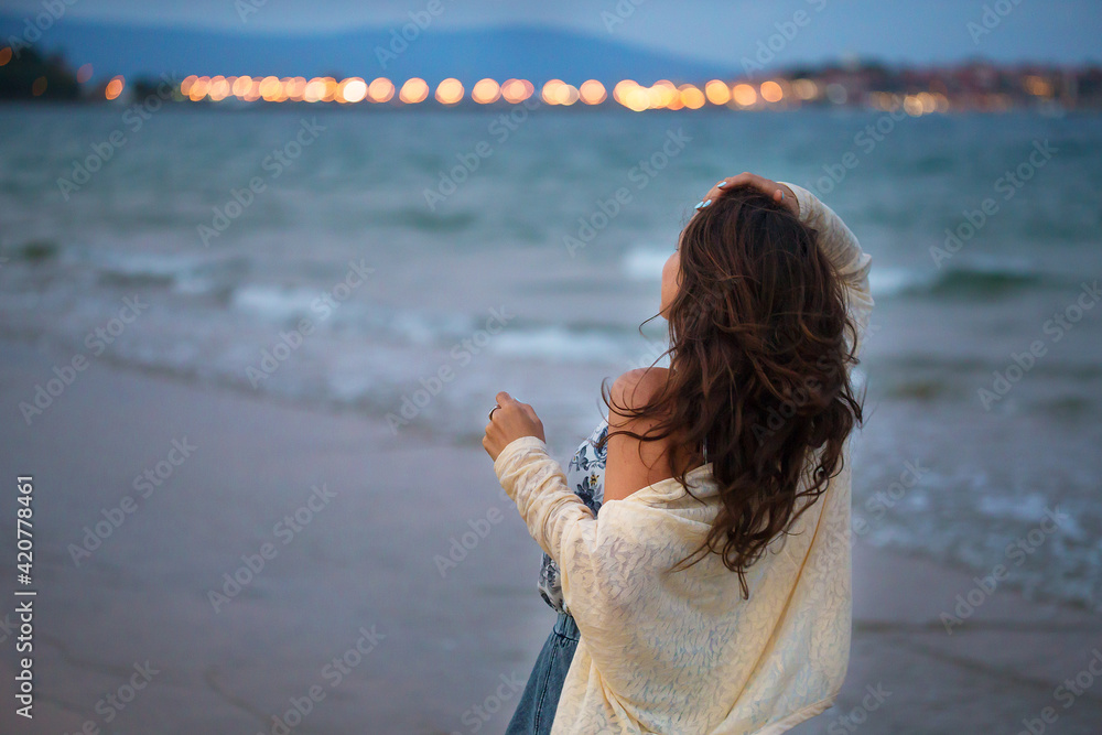 Obraz premium Girl looks at the sea and the city at sunset