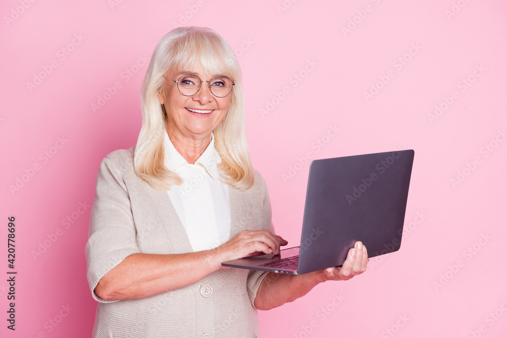 Photo of cheerful old woman hold netbook wear eyewear beige cardigan isolated pastel pink color background Photo of cheerful old woman hold netbook wear eyewear beige cardigan isolated pastel pink color background