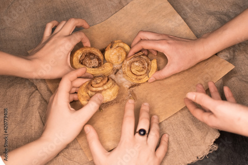 Many hands reaching for tasty cinnamon cinnabon buns or rolls on paper and linen background