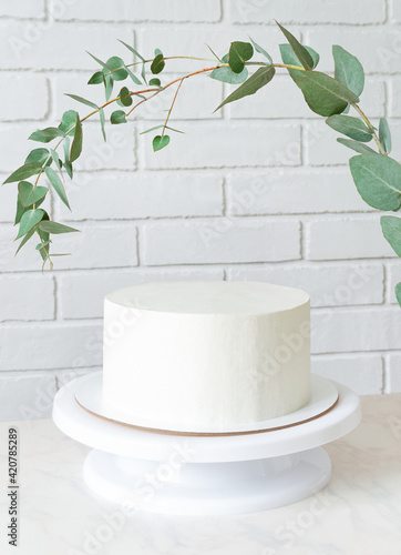 white cake without decor on a stand under a sprig of eucalyptus. cake with copy space