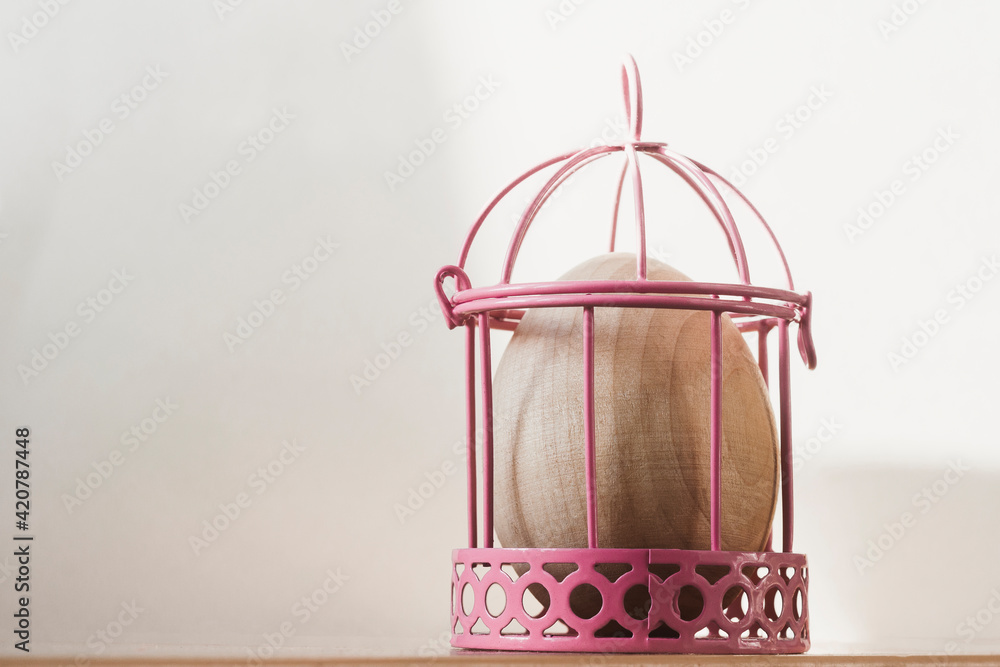 A wooden egg in a pink cage. The concept of the Easter holiday.