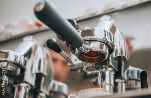 Closeup of fresh coffee pouring into a white ceramic cup from the shiny metal portafilter on an espresso machine