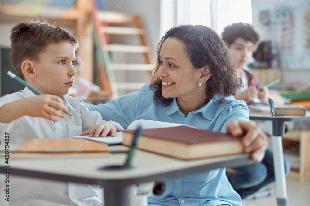 Happy kind teacher is helping kids in elementary school lessons Happy kind teacher is helping kids in elementary school lessons