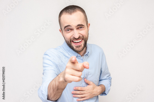 Bearded man laughs and points at you with his finger, white background, copy space