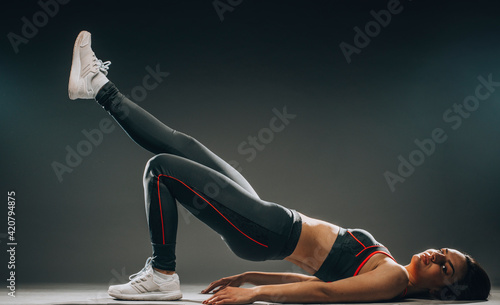 The muscular young woman athlete stretching on gray background.