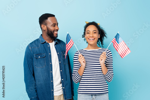 smiling african american man looking at happy wife holding small flags of usa on blue photo