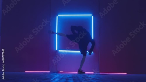 Person in windbreaker and red cap dancing to breakdance. blue rectangle neon background . Flickering neon background . man dancing to breakdance in night club