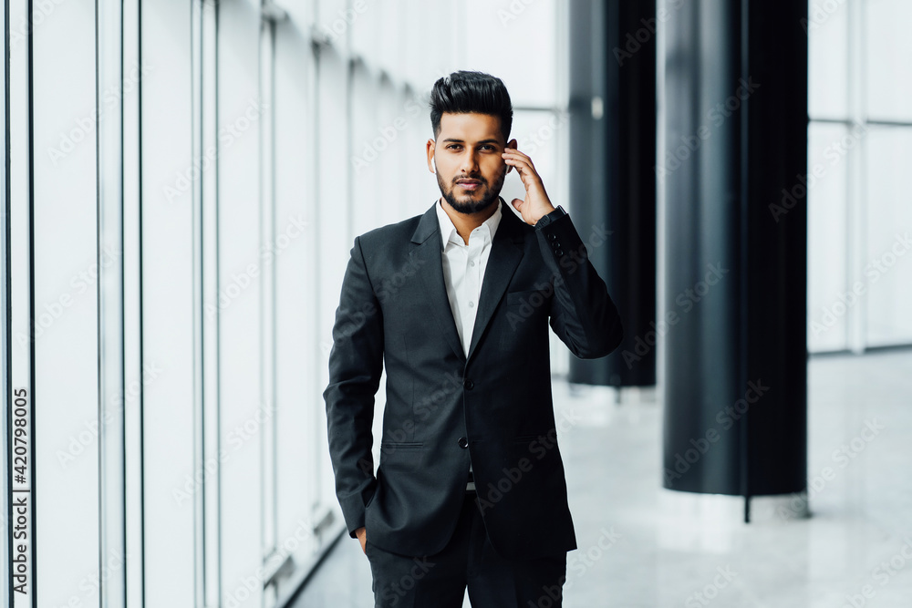 A bearded man of Asian appearance, an Indian male lawyer in a black suit touches wireless headphones and looks into the camera A bearded man of Asian appearance, an Indian male lawyer in a black suit touches wireless headphones and looks into the camera