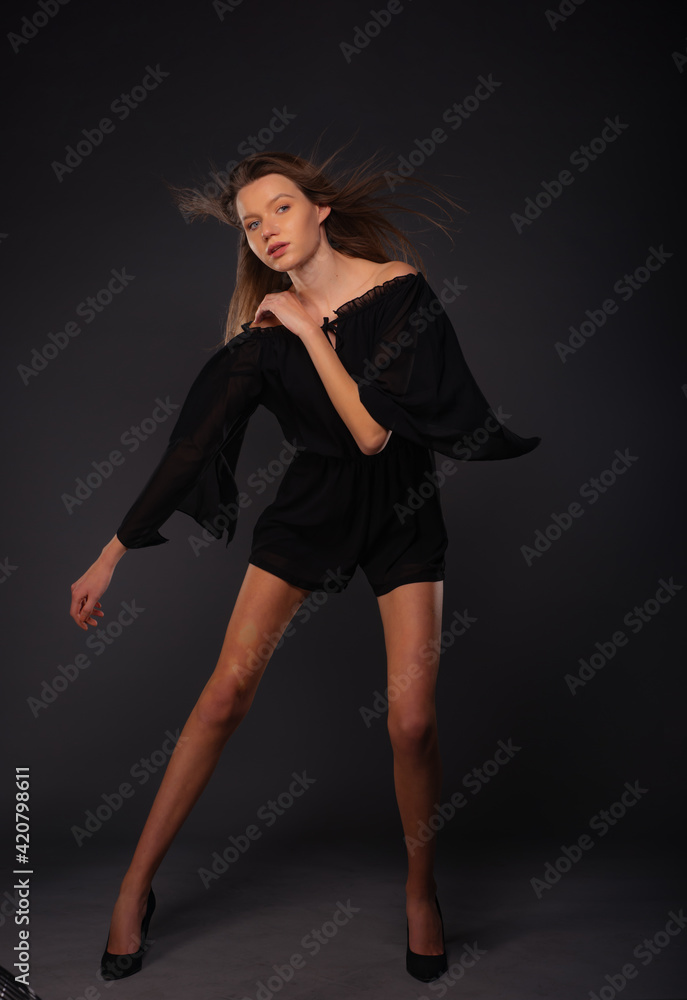 Full-length picture of an attractive sexy young female model posing isolated on a dark background with black dress Full-length picture of an attractive sexy young female model posing isolated on a dark background with black dress