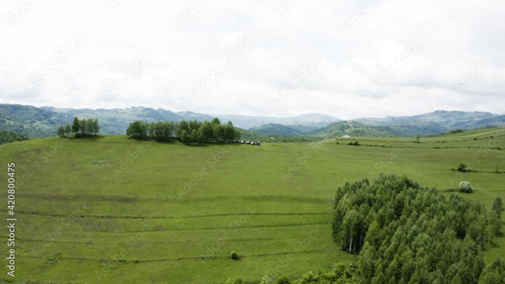 Aerial shot of multiple cars driving through remote countryside roads. Scenic green hilltops Aerial shot of multiple cars driving through remote countryside roads. Scenic green hilltops