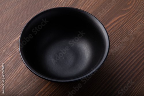 Empty black ceramic bowl isolated on wooden background. Close-up