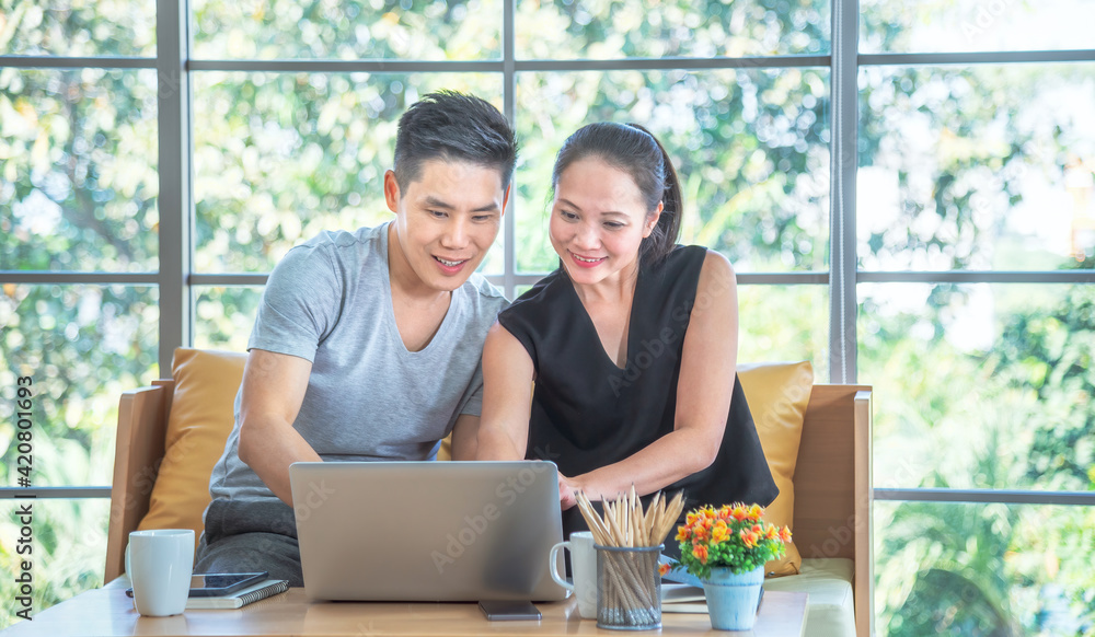 Beautiful young asian couple using laptop on the sofa at home. Young man working from home on laptop. Woman is smiling at her. Happy couple enjoying work from home Beautiful young asian couple using laptop on the sofa at home. Young man working from home on laptop. Woman is smiling at her. Happy couple enjoying work from home