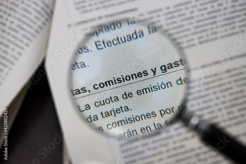 A magnifying glass points to the Spanish words commissions, fees and expenses on a bank document photo