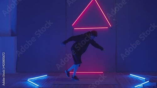 Person in windbreaker and red cap dancing to breakdance. red triangle neon background . Flickering neon background . man dancing to breakdance in night club