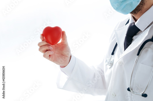 doctor in a protective mask holds a red heart in his hands.