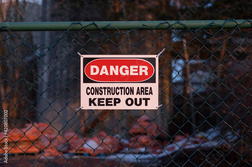 Sign danger construction area keep out on the fence, blurred background. Workplace hazards and safety concept.