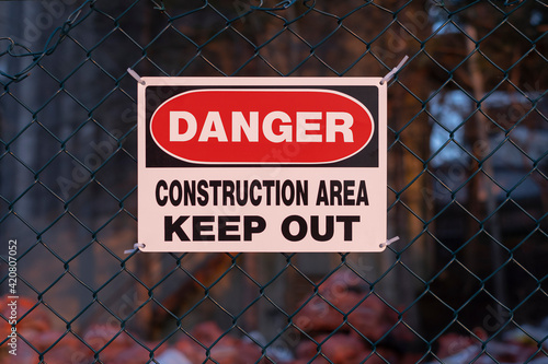 Sign danger construction area keep out on the fence, blurred background. Workplace hazards and safety concept.