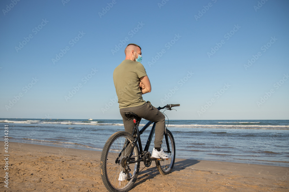 Boy with green shirt and mask arriving at his destination after a bike ride to rest on the beach Boy with green shirt and mask arriving at his destination after a bike ride to rest on the beach