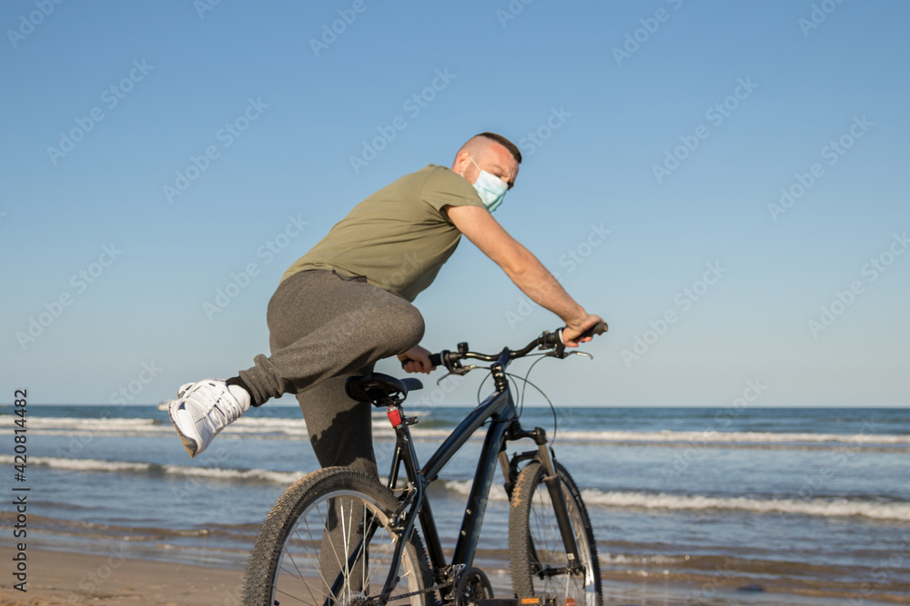 Obraz premium Boy with green shirt and mask arriving at his destination after a bike ride to rest on the beach