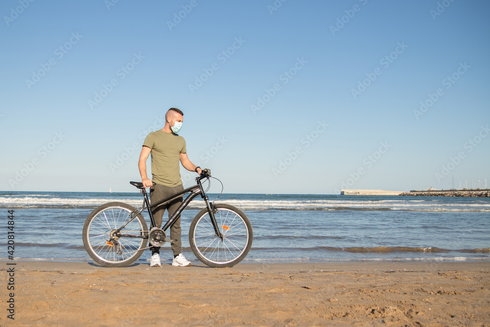 Boy with green shirt and mask arriving at his destination after a bike ride to rest on the beach