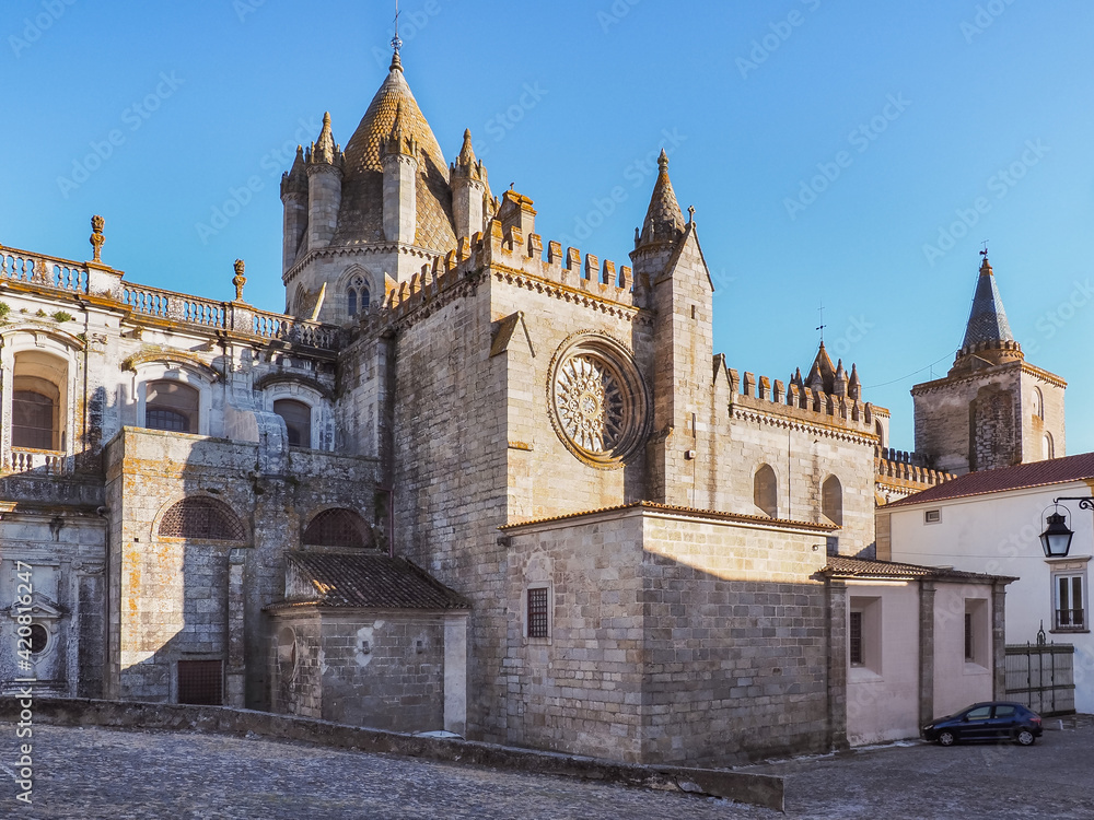 Side view of massive Roman catholic church or Cathedral of Evora known as Sé de Évora. Beautiful ancient, masonry of rose granite stone, building, with conical main lantern-tower and wall battlements.