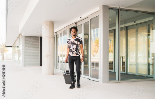 Tourist man carrying suitcase while walking outdoors. © Mego-studio