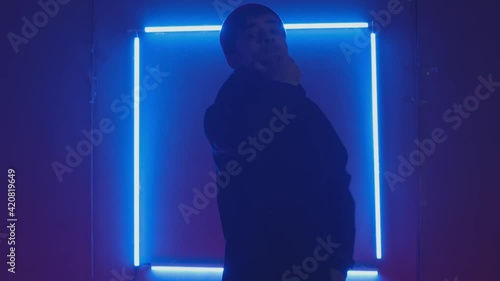 Person in windbreaker and red cap dancing to breakdance. blue rectangle neon background . Flickering neon background . man dancing to breakdance in night club