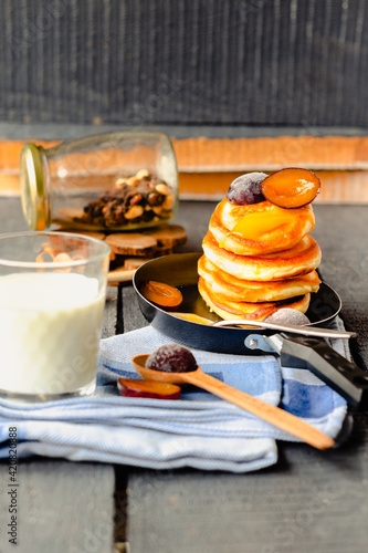Morning breakfast. pancakes with a sweet plum and honey in a frying pan on a blue wooden background. a glass of milk. rustic style.copy space for text