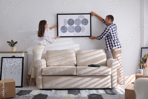 Happy couple hanging picture on white wall together. Interior design