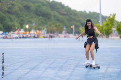 Asian woman playing surf skate or skates board outdoors on beautiful summer day. Happy young women play surf skate at park on morning time in the park.