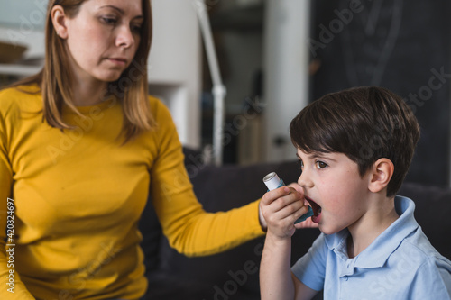 boy using asthma pump. his mother is beside him