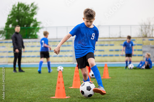 Boys attending soccer training on school field. Young man coaching children on physical education class. Soccer practice for children © matimix
