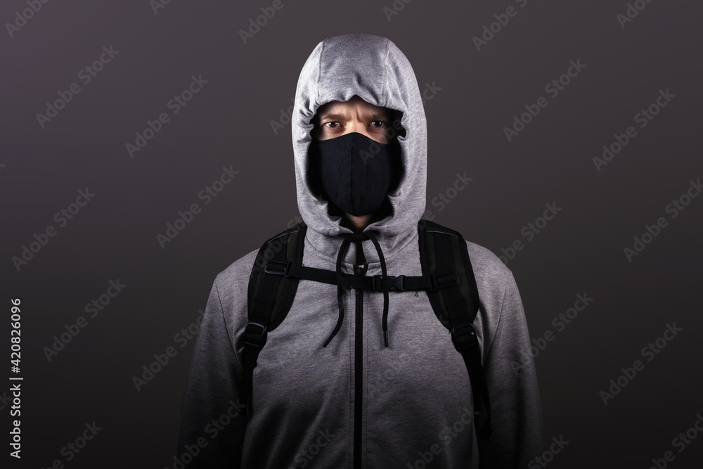 A male stalker in mask, wearing a hooded jacket on his head looks into the camera, isolated A male stalker in mask, wearing a hooded jacket on his head looks into the camera, isolated