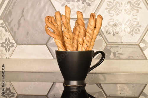Several grissini breadsticks in a black cup, close-up, on a background of tiles.