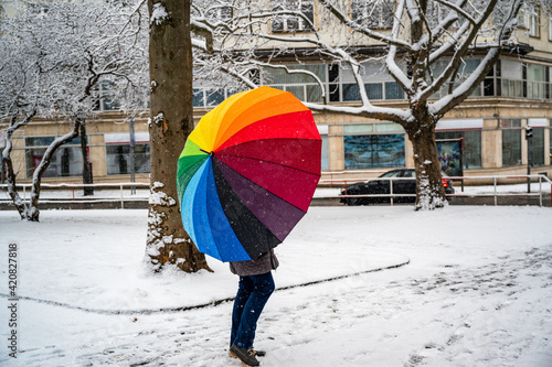 Woman with rainbow umbrella walking down snow-covered street.