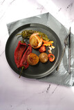 Baked potatoes, garlic, carrots, cherry tomatoes and capia peppers on a black porcelain plate.