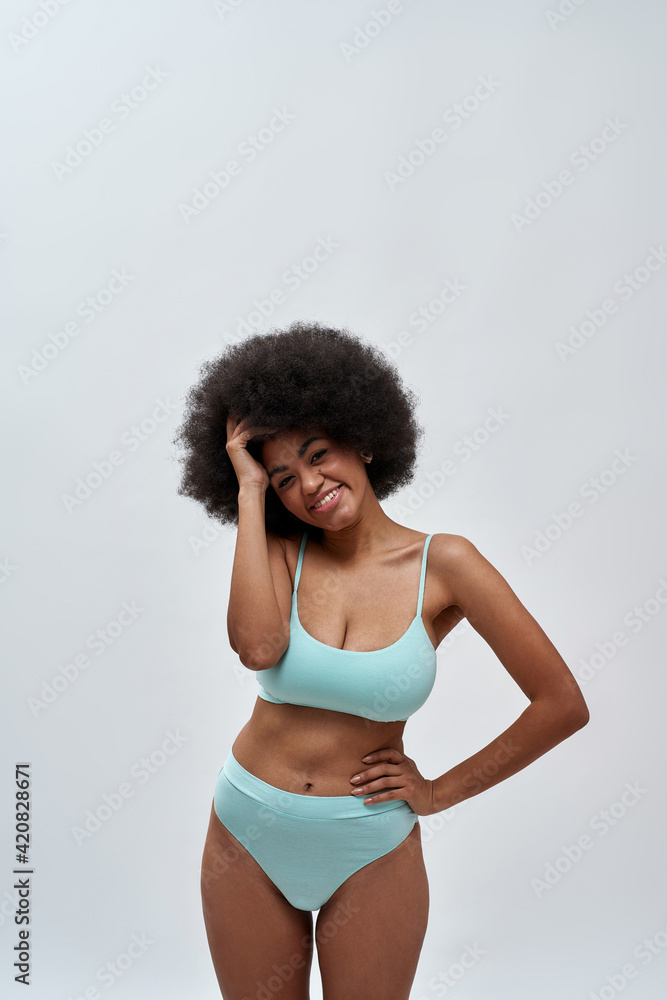 Excited curvy young female model with afro hair style wearing blue  underwear smiling at camera, posing isolated over light background Photos |  Adobe Stock