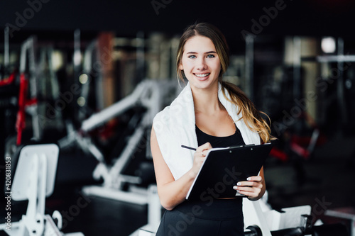 Smiling attractive woman personal trainer is waiting for you for a workout! she holds a notebook in her hands and smiles at the camera